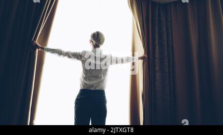 Eine Geschäftsfrau öffnete morgens die Vorhänge im Hotelzimmer und schaute ins Fenster Stockfoto