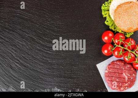 Die Zutaten für den hausgemachten Burger. Rohe Dose, Tomaten, Käse, Salat, Weizenbrötchen auf schwarzem Schieferhintergrund auf der rechten Seite mit Copy Spa Stockfoto