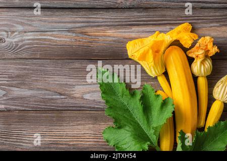 Frische gelbe Zucchini oder Squash mit Blumen auf Holzgrund. Draufsicht mit Kopierbereich. Frisch geerntetes Gemüse Stockfoto