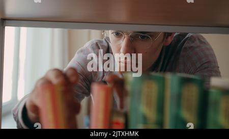 Junge ernsthafte kaukasischen schönen männlichen Studenten steht vor dem Bücherregal in der Universität leicht geräumige Bibliothek auf der Suche nach Lehrbuch Stockfoto