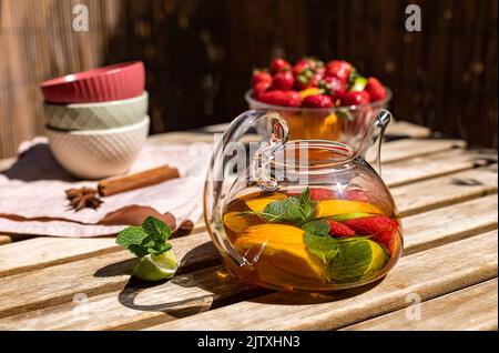 Roter Früchtetee mit Beeren in einer Glas-Teekane auf dem sonnigen Balkon. Stockfoto