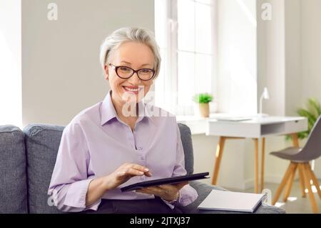 Glückliche, schöne, lächelnde, reife Geschäftsfrau mit Brille und modernem Tablet-Computer Stockfoto