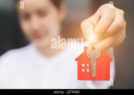 Immobilienmakler, der den Hausschlüssel auf dem hausförmigen Schlüsselbund hält, Modellhaus. Konzept der Investitionsimmobilie. Stockfoto