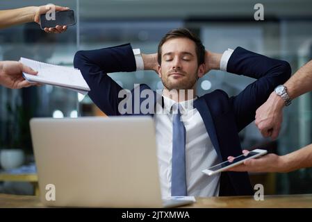 Ruhiger Umgang mit Unternehmensanforderungen. Aufnahme eines Geschäftsmanns, der ruhig an seinem Schreibtisch sitzt, während er von anspruchsvollen Kollegen in einem Büro umgeben ist. Stockfoto