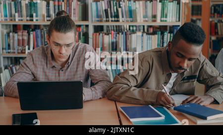 Zwei konzentrierte Studenten, die sich auf die Prüfung vorbereiten, während sie in der Universitätsbibliothek an einem Tisch sitzen Stockfoto