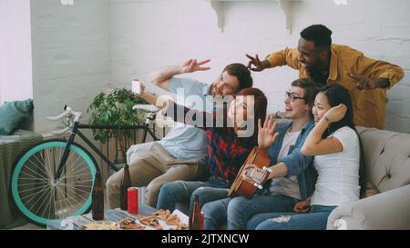 Eine Gruppe von fröhlichen Freunden, die Selfie-Fotos mit der Smartphone-Kamera machen, während sie zu Hause auf der Party mit Bier und Snacks feiern Stockfoto