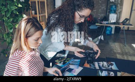 Kreative Kollegen, die Bilder auf den Tisch legen und flache Lay-Aufnahmen machen, während sie über die Projektgestaltung sprechen. Draufsicht des modernen Tisches mit Illustrationen, Notizbüchern und Markern. Stockfoto