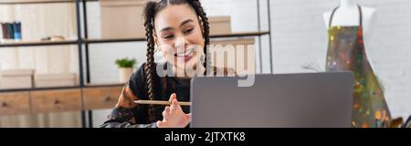 afroamerikanischer Designer mit Bleistift mit Videoanruf auf Laptop in Werkstatt, Banner, Stock Bild Stockfoto