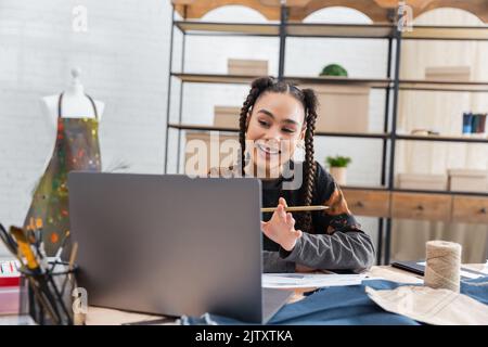 Lächelnde afroamerikanische Kunsthandwerkerin mit Videoanruf auf dem Laptop in der Werkstatt, Stockbild Stockfoto
