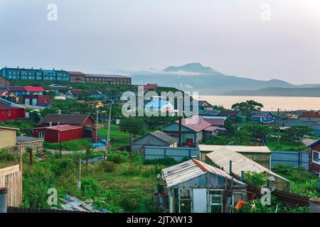 Landschaft der Stadt Yuzhno-Kurilsk auf der Insel Kunashir mit Blick auf die Meeresbucht und den Mendelejew-Vulkan in der Ferne Stockfoto