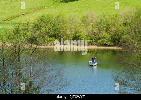 Ein Mann, der im Frühjahr von einem Boak auf dem Clatworthy Reservoir an den Südhängen der Brendon Hills, Somerset, England, fischt. Stockfoto