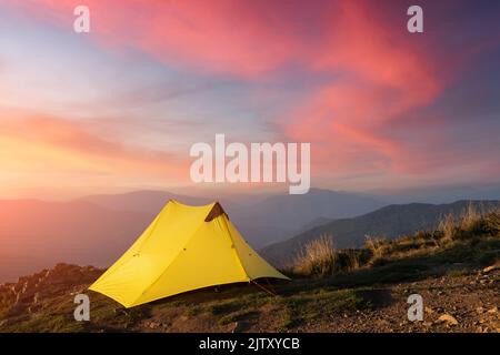 Gelbes Zelt vor dem Hintergrund einer unglaublichen Berglandschaft während eines wunderschönen Sonnenuntergangs. Unglaubliches Hochland. Tourismuskonzept Stockfoto