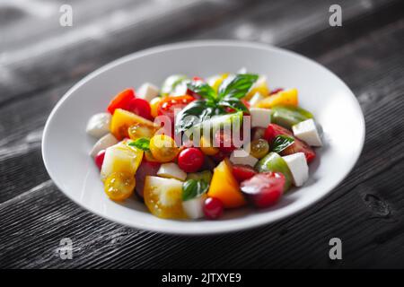 Salat mit verschiedenen Sorten, rote, gelbe, grüne und schwarze Tomatenmischung, Mozzarella-Käse und Basilikum. Caprese Salas mit frischen bunten Tomaten. Food-Fotografie Stockfoto