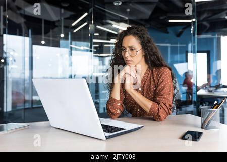 Nachdenkliche und fokussierte weibliche Programmierer Web-Entwickler arbeiten in modernen Produktentwicklung Unternehmen Hispanic Frau sitzen und denken mit Laptop, um Code zu schreiben. Stockfoto