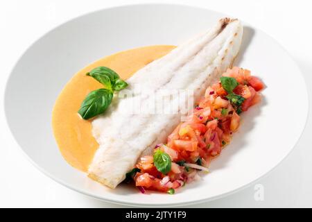 Gegrilltes Seebarschfilet mit Tomaten-Basilikumsalat und Soße auf Weiß Stockfoto