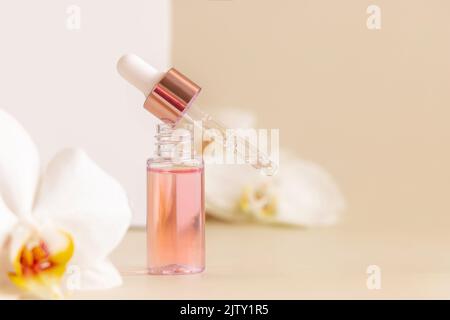 Hellrosa geöffnete Tropfflasche mit Serum und einer Pipette in der Nähe von weißen Orchideenblüten auf hellbeige, Nahaufnahme, Kopierraum. Hautpflege kosmetisches Produkt, e Stockfoto