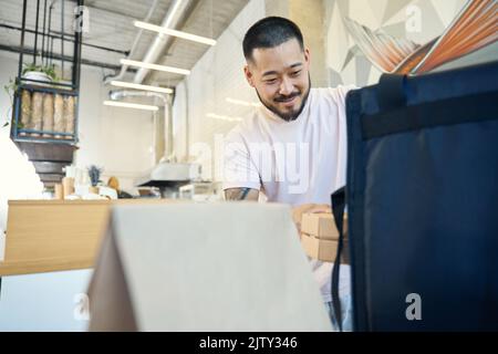 Ein fröhlicher junger Mann, der das Essen aus dem Café angeliefert hat Stockfoto