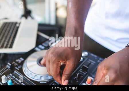Blick auf DJ-Mixer und Vinylplatte mit Kopfhörern auf einem Tisch mit afroamerikanischem DJ auf der Bühne und mischt den Track im Hintergrund, während su Stockfoto