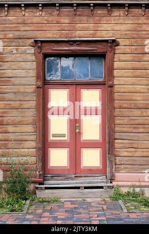 Alte rote Holztüren, Eingang zum Holzhaus mit vertrocknender brauner Farbe an den Wänden in Tartu, Estland. Stockfoto