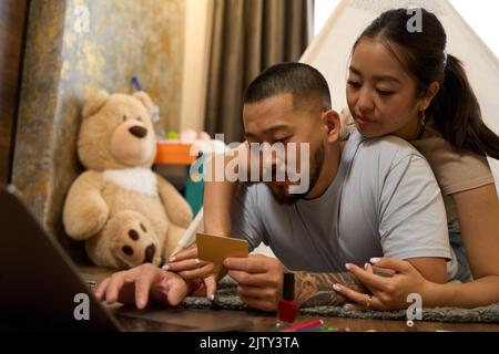 Nettes asiatisches Paar sitzen auf dem Boden vor dem Laptop Stockfoto