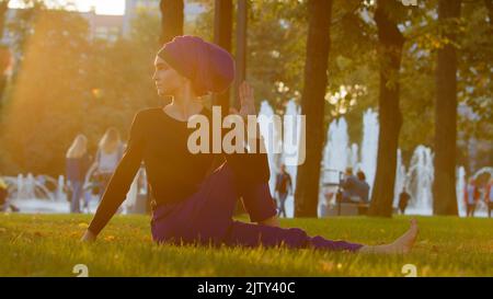 Starke islamische muslimische indische Frau in Hijab aktiv Mädchen tun Yoga im Park im Freien Training Übungen anspannen Muskeln zeigen akrobatische Elemente Stockfoto