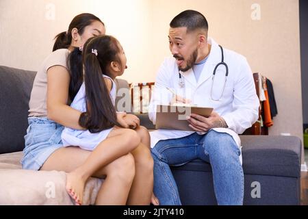 Die Ärztin untersucht die kleine Patientin, die in den Armen ihrer Mutter sitzt Stockfoto