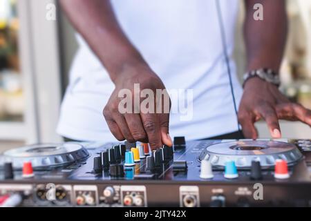 Blick auf DJ-Mixer und Vinylplatte mit Kopfhörern auf einem Tisch mit afroamerikanischem DJ auf der Bühne und mischt den Track im Hintergrund, während su Stockfoto