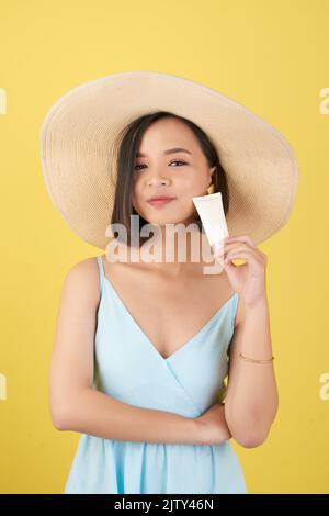 Schöne junge Frau in Strohhut mit einer Flasche Sonnencreme Stockfoto