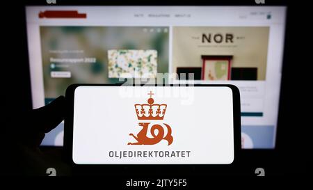 Person, die das Smartphone mit dem Logo der Agentur Norwegian Petroleum Directorate (NPD) auf dem Bildschirm vor der Website hält. Konzentrieren Sie sich auf die Telefonanzeige. Stockfoto