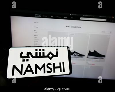Person, die Mobiltelefon mit dem Logo des arabischen E-Commerce-Unternehmens Namshi auf dem Bildschirm vor der Business-Webseite hält. Konzentrieren Sie sich auf die Telefonanzeige. Stockfoto