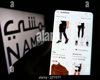 Person, die Mobiltelefon mit der Webseite des arabischen E-Commerce-Unternehmens Namshi auf dem Bildschirm vor dem Unternehmenslogo hält. Konzentrieren Sie sich auf die Mitte des Telefondisplays. Stockfoto