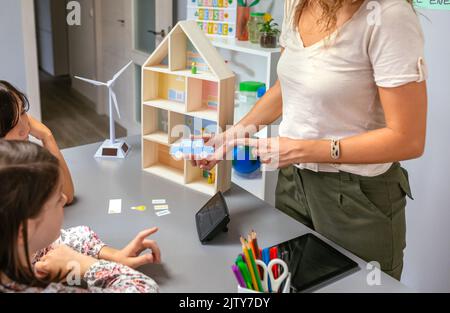 Die Lehrerin erklärt ihren Schülern die Teile eines nachhaltigen Hauses mit einem Elektroauto Stockfoto