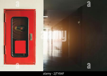 Feuerlöscher und Feuerschlauchtrommel im Hotel, Brandschutzausrüstung auf Wandzement Stockfoto