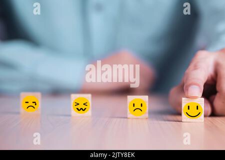 Geschäftsmann wählt ein Lächeln Emoticon Symbole Gesicht glücklich Symbol auf Holzblock , Dienstleistungen und Kundenzufriedenheit Umfragekonzept Stockfoto