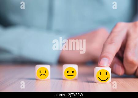 Geschäftsmann wählt ein Lächeln Emoticon Symbole Gesicht glücklich Symbol auf Holzblock , Dienstleistungen und Kundenzufriedenheit Umfragekonzept Stockfoto