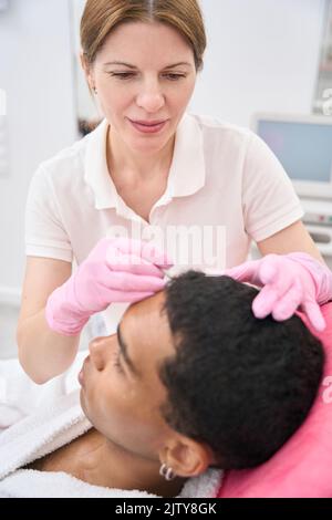 Kosmetologe, der Markierungen auf dem Behandlungsbereich auf dem Gesicht eines jungen Mannes platziert Stockfoto