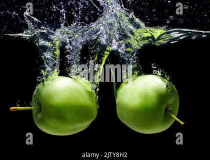 Grüne Äpfel fielen in Wasser, Spritzer und Blasen isoliert auf schwarzem Hintergrund, Nahaufnahme Stockfoto