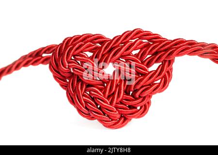 Roter herzförmiger Knoten aus Kordel mit Gewinde, isoliert auf weißem Hintergrund. Kreatives romantisches Konzept. Stockfoto