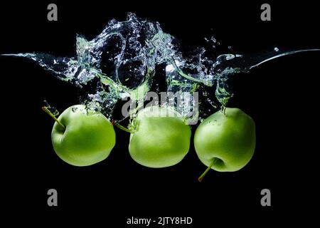 Gruppe von grünen Äpfeln unter Wasser geworfen mit Spritzern vor schwarzem Hintergrund. Stockfoto