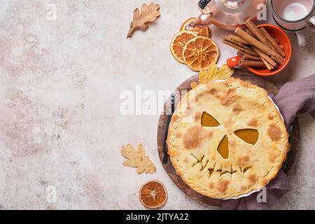 Halloween-Essen. Hausgemachter Kürbiskuchen oder Torte mit einem gruseligen Gesicht für Halloween auf einem Holztisch. Speicherplatz kopieren. Halloween-Food-Konzept. Stockfoto