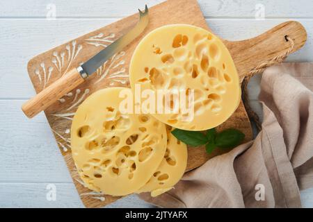 Käse Maasdam oder Radamer. Stück Käse auf Holzstandbrett auf weißem Holztisch Hintergrund. Draufsicht. Freier Speicherplatz für Ihren Text. Stockfoto