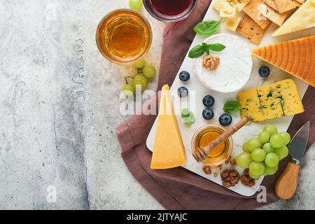 Auswahl an Käse, Honig, Cracker, Heidelbeeren, Trauben mit Rot-und Weißwein in Gläsern Antipasto Server auf weißem Marmorbrett auf grauem Hintergrund Stockfoto