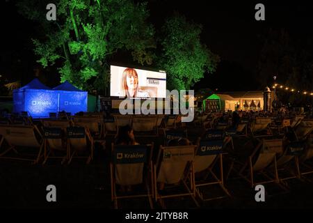 Krakau, Polen - 19. August 2022: Ein offenes Kino oder ein Film, der einen Dokumentarfilm für die Öffentlichkeit in der Nacht projiziert, bei dem mehrere Menschen zuschauen Stockfoto