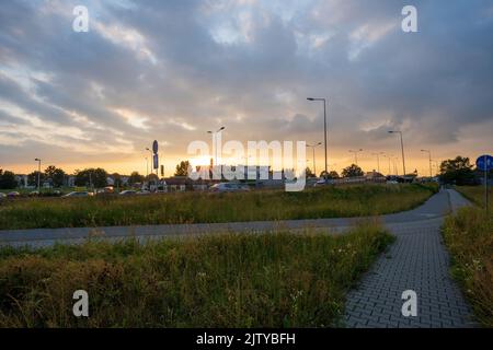 Ein Blick auf einen betonierten Bürgersteig mit Wegen, die für Fußgänger- und Fahrradverkehr bestimmt sind, die sich auf einem mittleren Abschnitt gegen den Verkehr und dramatische Wolken verbinden Stockfoto