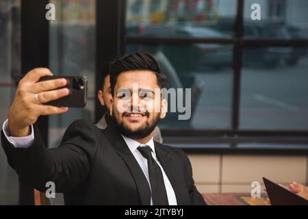 Freunde Geschäftspartner machen ein Selfie bei einem Meeting. Eine internationale Gruppe von Männern in Anzügen sitzt an einem Tisch im Freien und redet. Arbeitsmomente und Stockfoto