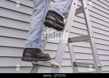 Männlicher Arbeiter klettert vor dem Hausliding auf die Stube Stockfoto