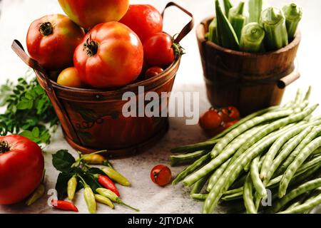 Stillleben von frischem hausgemachten Gemüse Kirschtomaten grüne Bohnen rote Paprika Chilis okra und Moringa Blätter Stockfoto