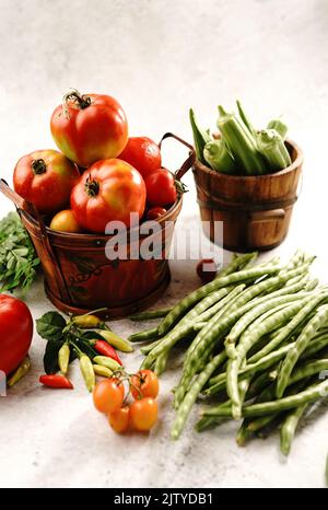 Stillleben von frischem hausgemachten Gemüse Kirschtomaten grüne Bohnen rote Paprika Chilis okra und Moringa Blätter Stockfoto