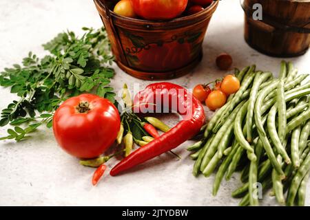 Stillleben von frischem hausgemachten Gemüse Kirschtomaten grüne Bohnen rote Paprika Chilis okra und Moringa Blätter Stockfoto