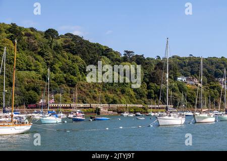 Dartmouth Heritage Eisenbahnlinie mit einer Dampfeisenbahn, die entlang des River Darts verläuft und Yachten im Vordergrund vor Anker liegen. Stockfoto